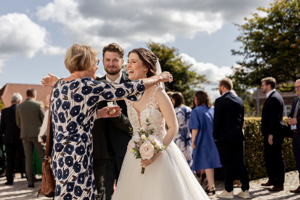 Wedding guests gather outside to celebrate during a sunny outdoor reception.