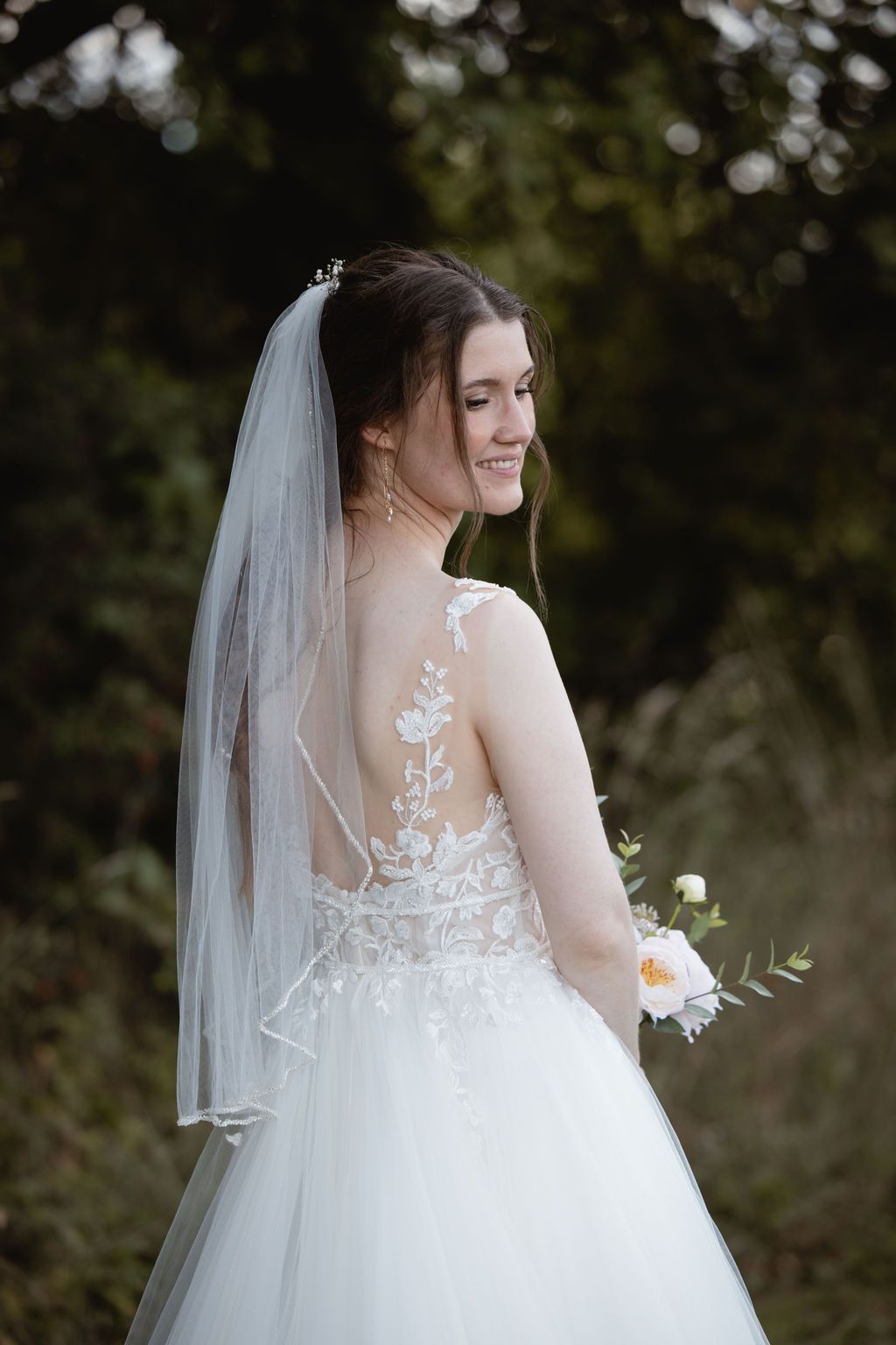 Back view of bride in lace detailed wedding gown with sheer illusion back and flowing veil.