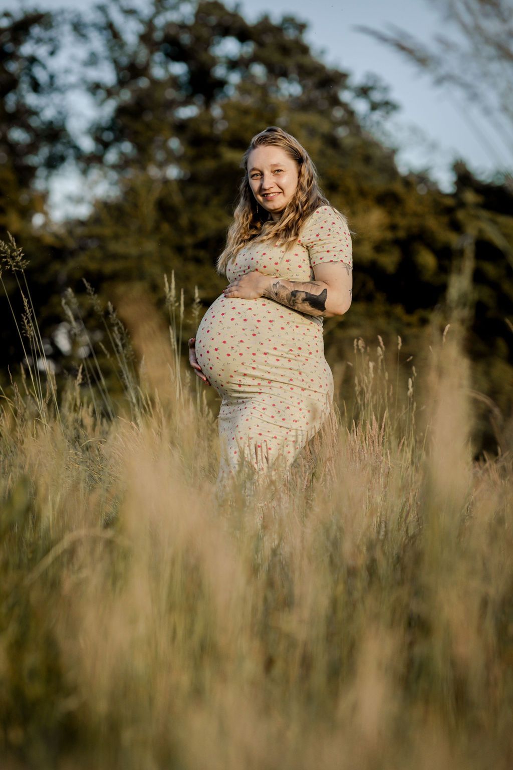 Woman in a cream polka dot dress poses among tall grass in a natural outdoor setting.