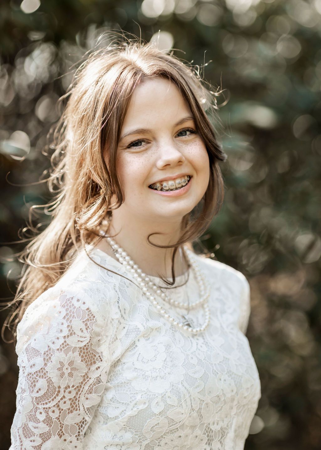 Person in vintage-style white lace dress poses with pearl necklace in natural lighting.