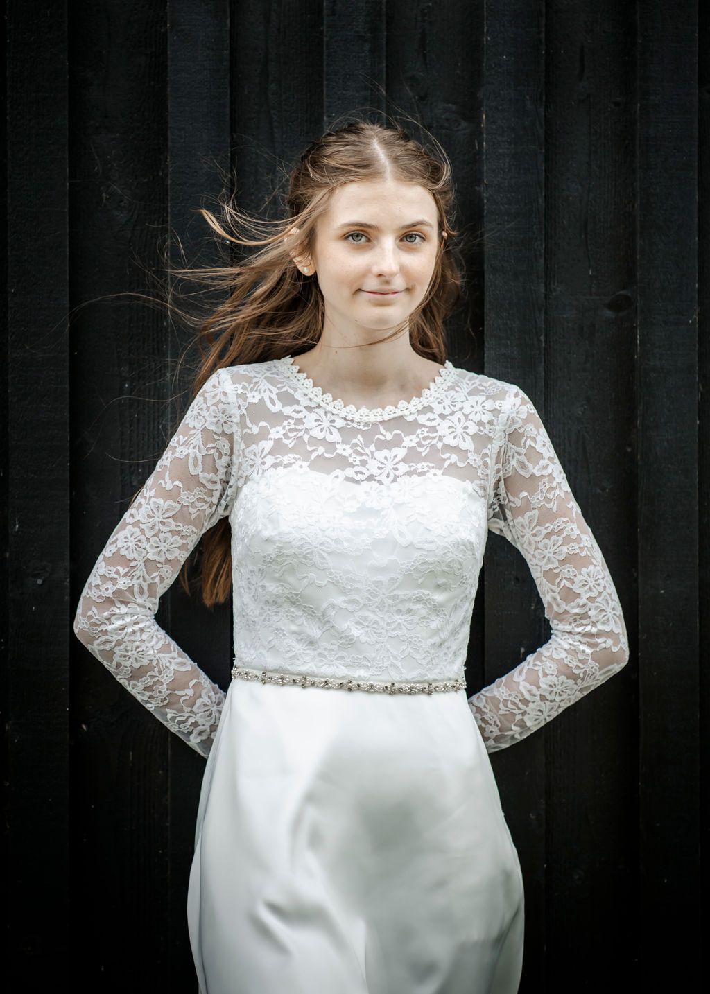 Wedding dress with lace bodice and long sleeves displayed against black background.