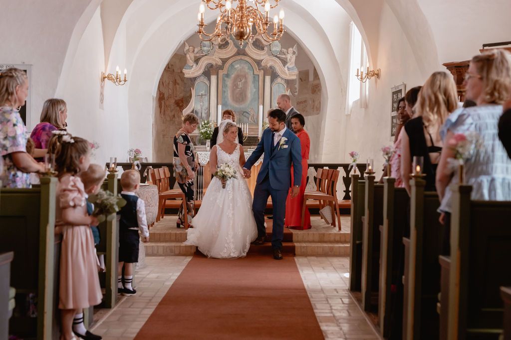 Wedding ceremony in elegant church with chandelier and wooden pews.