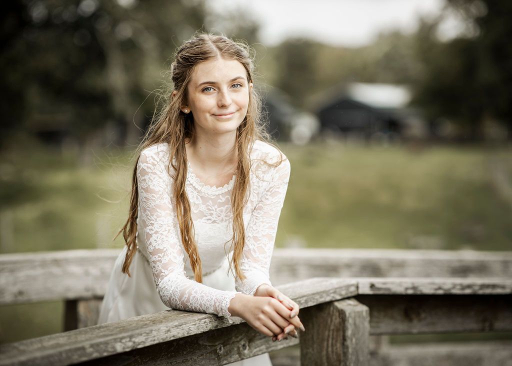 Outdoor bridal photography featuring white lace dress against rustic wooden fence.