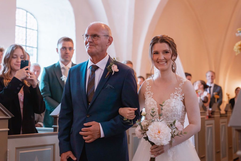 Wedding ceremony guests gather in an elegant church with vaulted ceilings and ornate architecture.