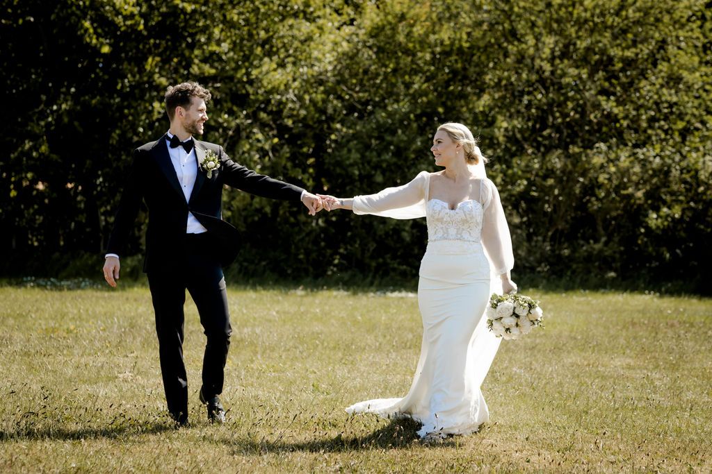A couple shares a romantic moment in their wedding attire on a sunny outdoor field.