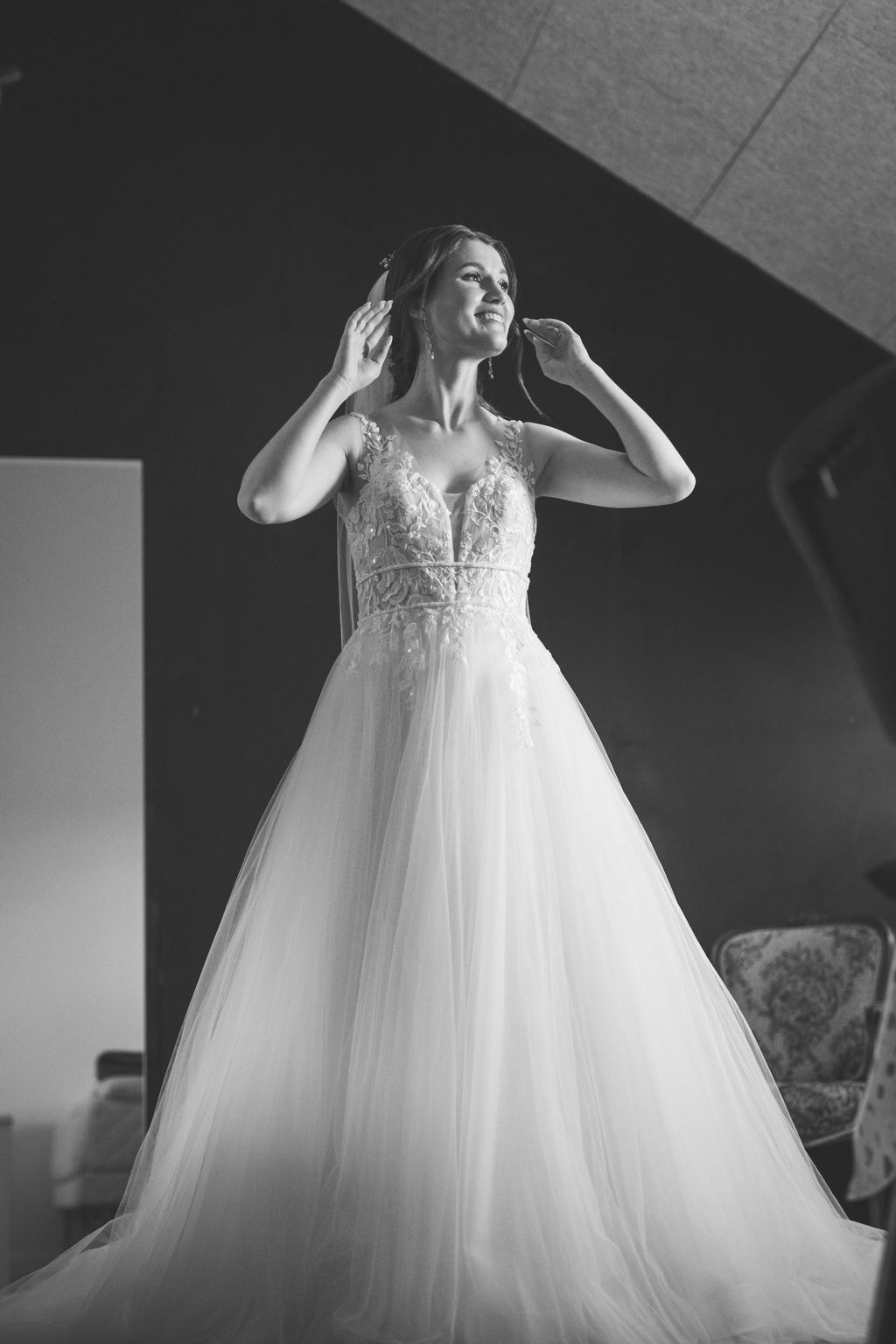 Black and white portrait of a bride in a flowing tulle wedding gown adjusting her veil.