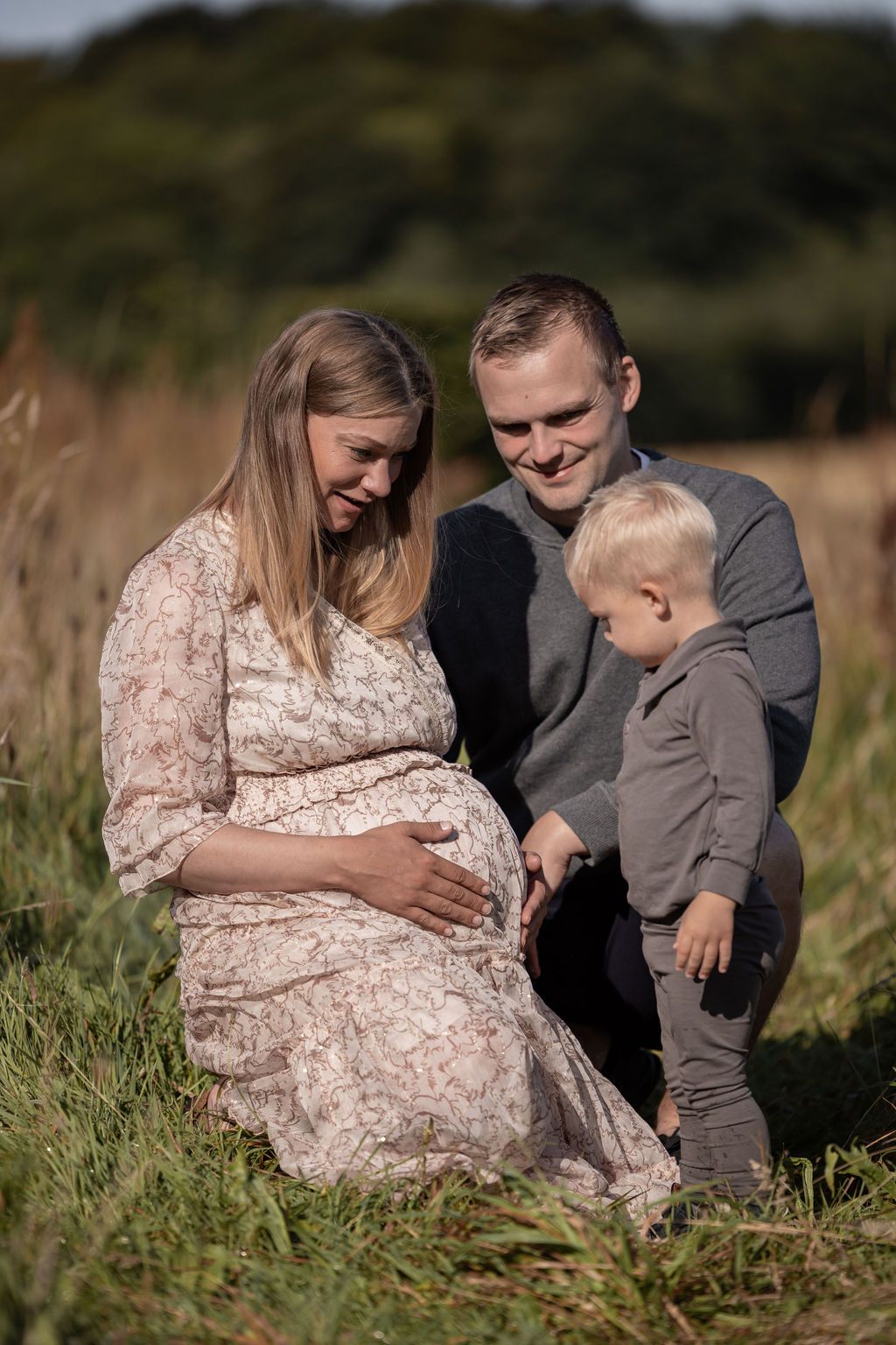 A tender family moment photographed in a natural outdoor setting with golden sunlight.