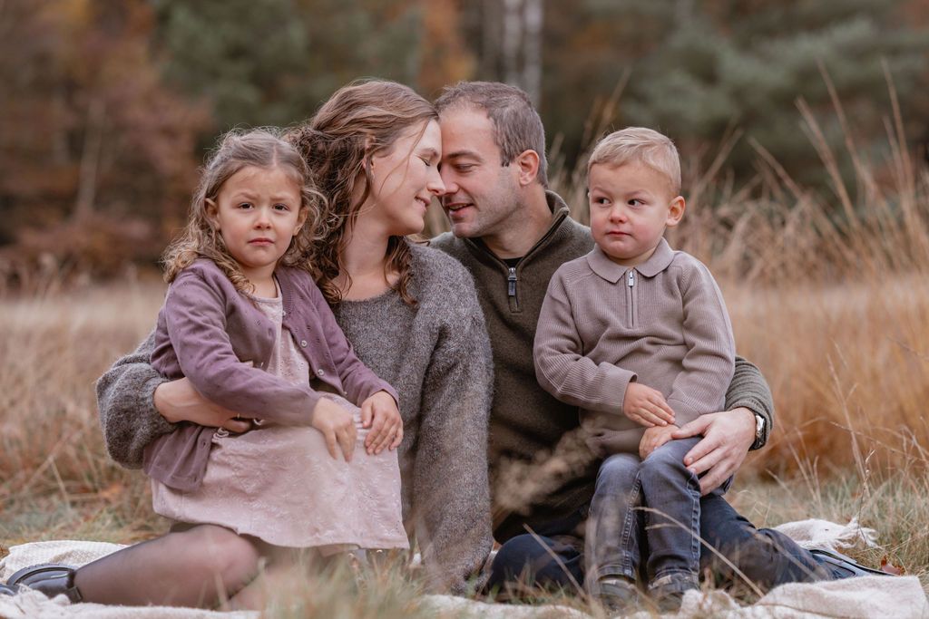 Family of four sits together on a blanket in tall autumn grass.