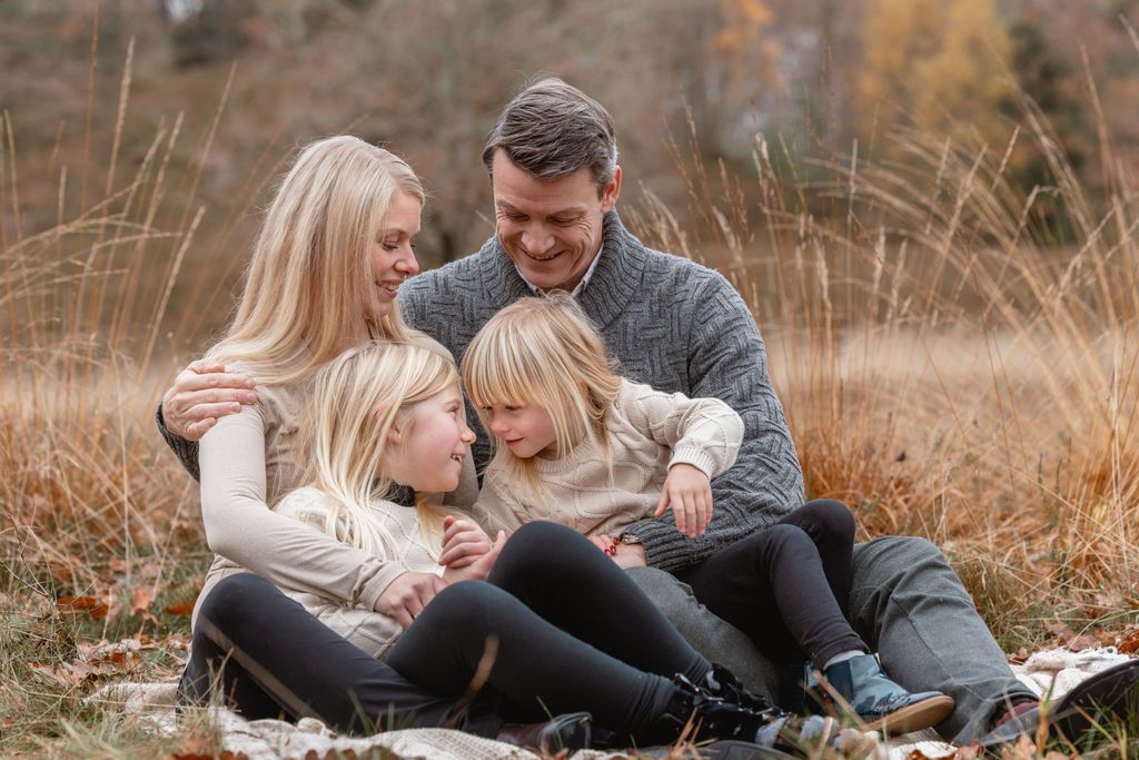 Family cuddles together on ground during autumn photoshoot outdoors.