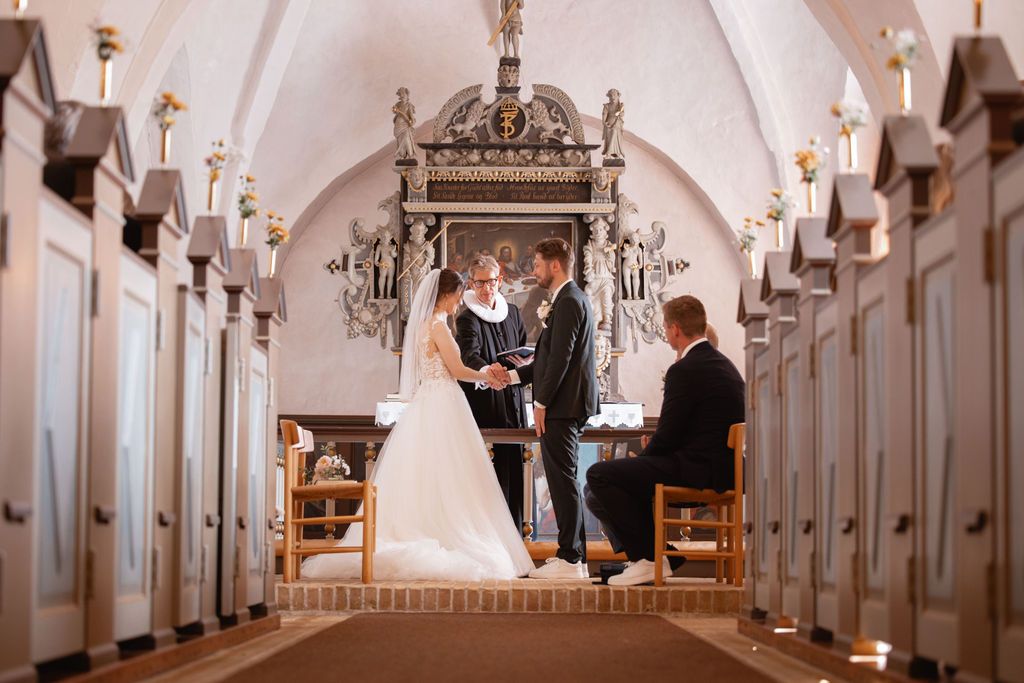 A wedding ceremony takes place in a beautiful church with vaulted ceilings and wooden pews.
