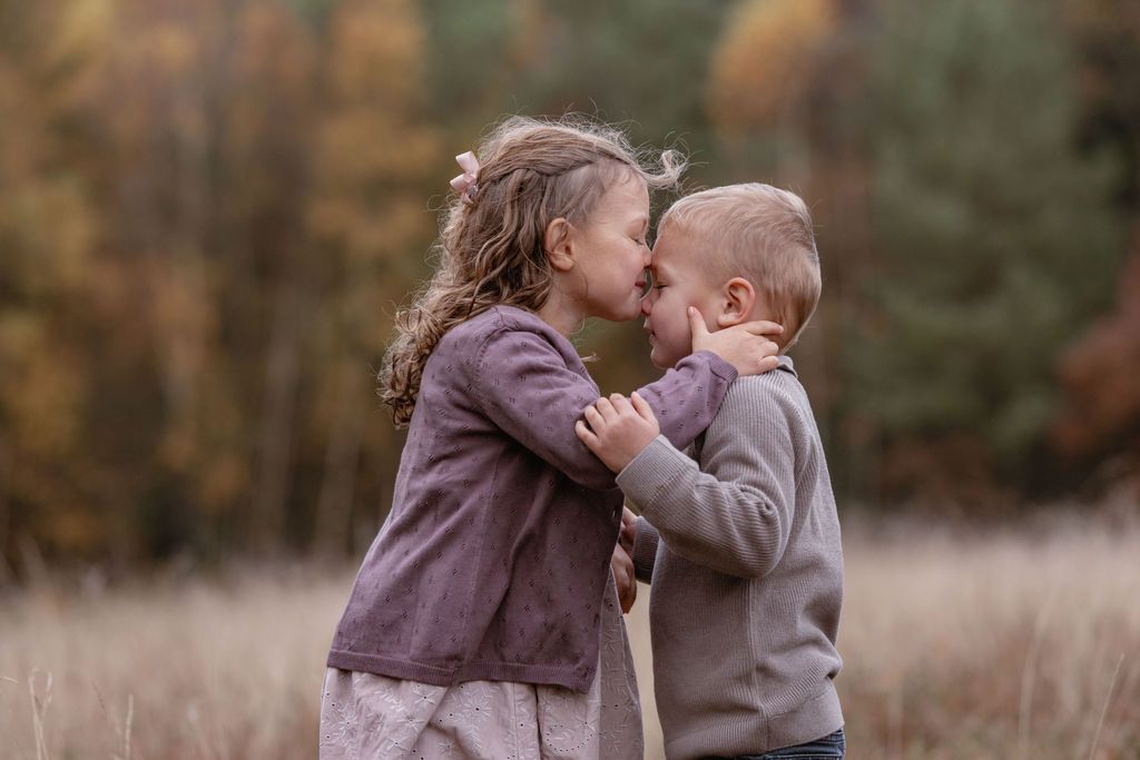 Two children share a sweet moment together in a field during autumn.