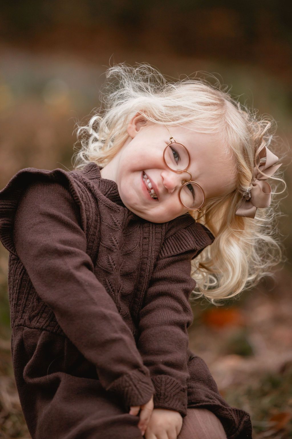Child in brown sweater playing with curly hair against autumn background.