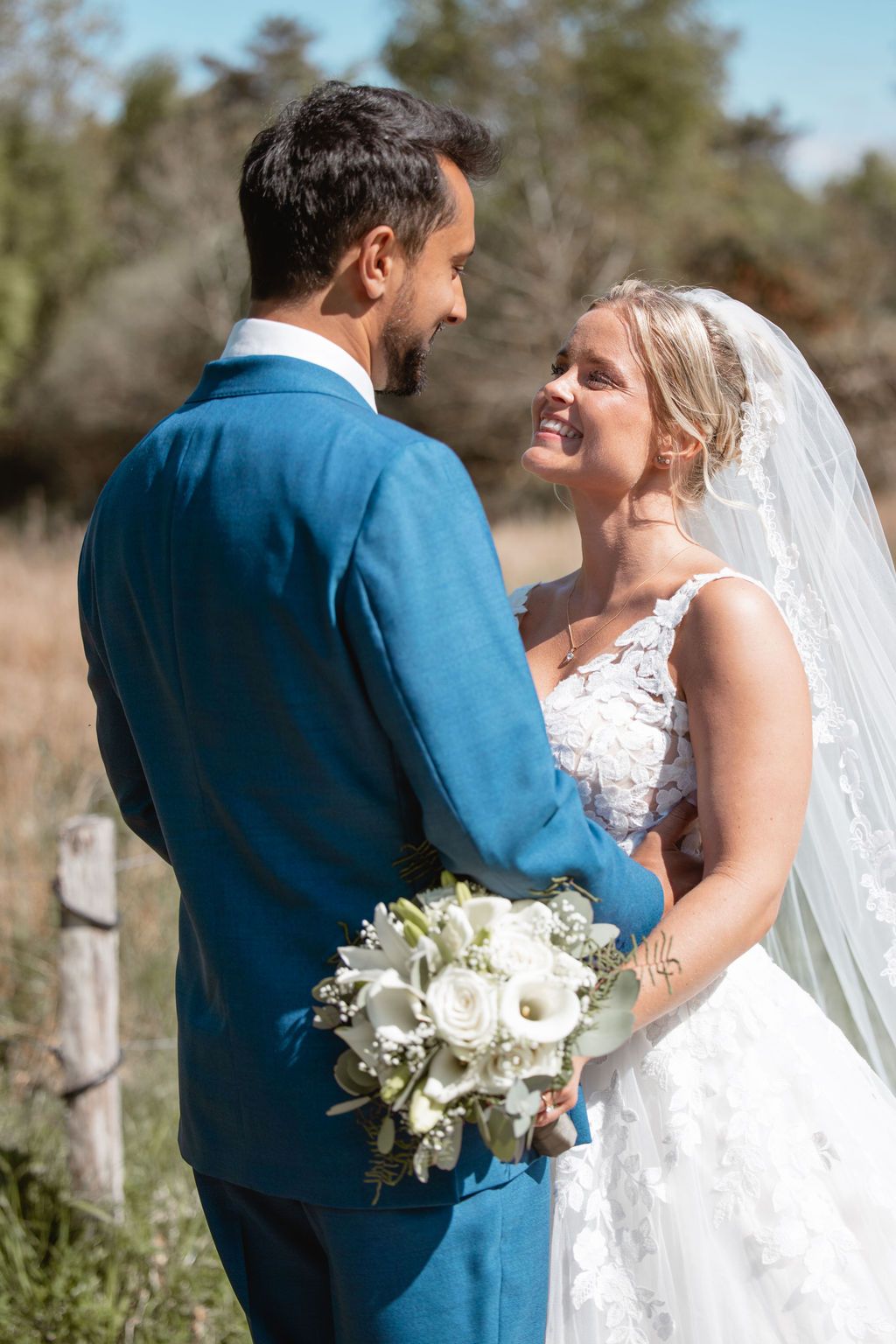 Romantic moment between newlyweds holding a white bouquet outdoors.