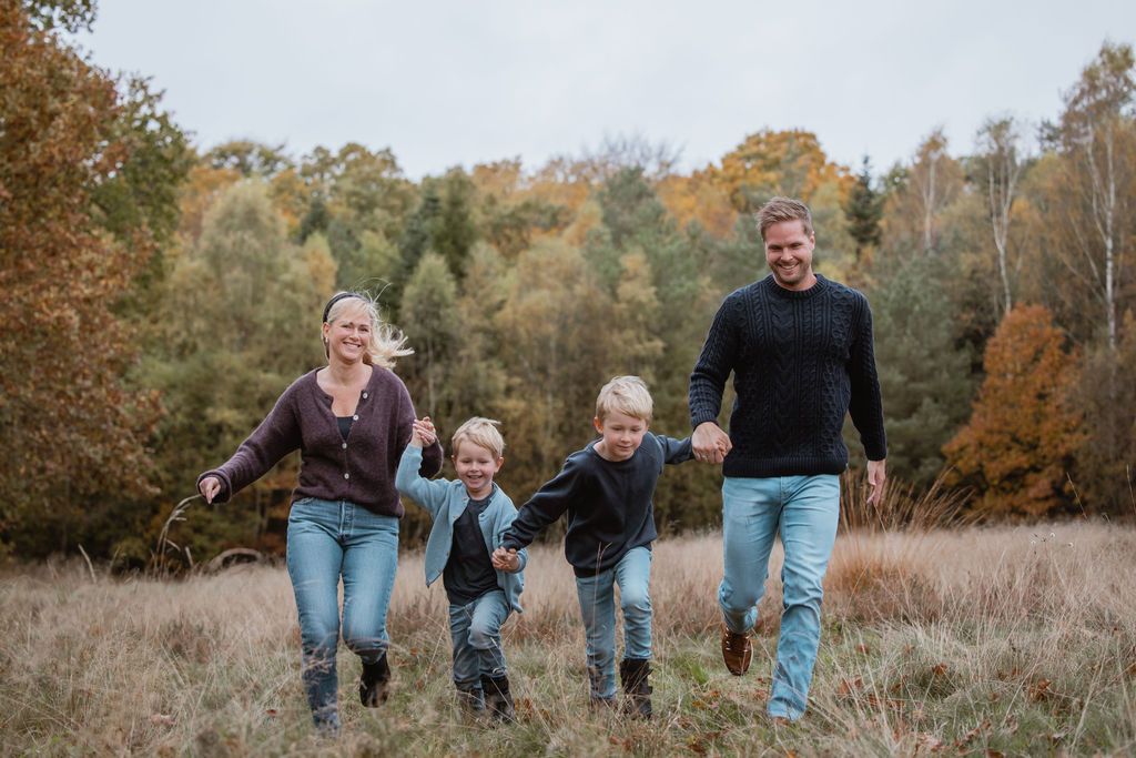 Casual family photoshoot with everyone walking through tall grass during fall.