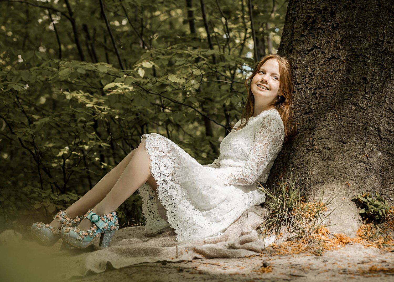 Person in white lace dress reclines against tree trunk in moody forest setting.