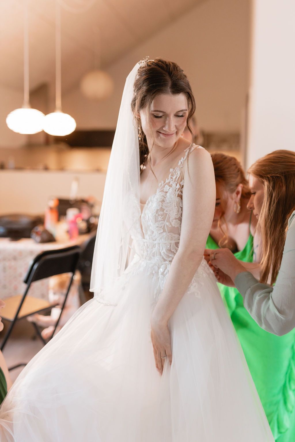 A bride in a full tulle wedding gown smiles during final dress preparations.