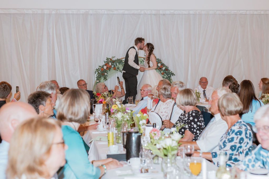 Wedding reception hall with guests seated at decorated tables.