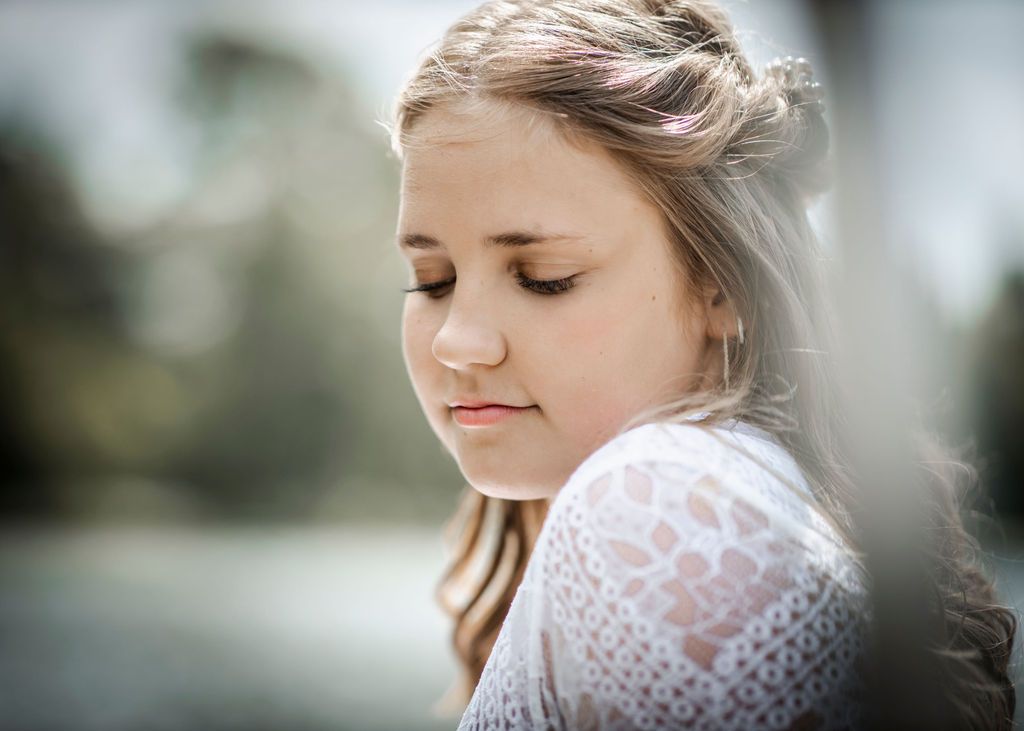 Person in delicate white lace dress poses outdoors with soft natural lighting.