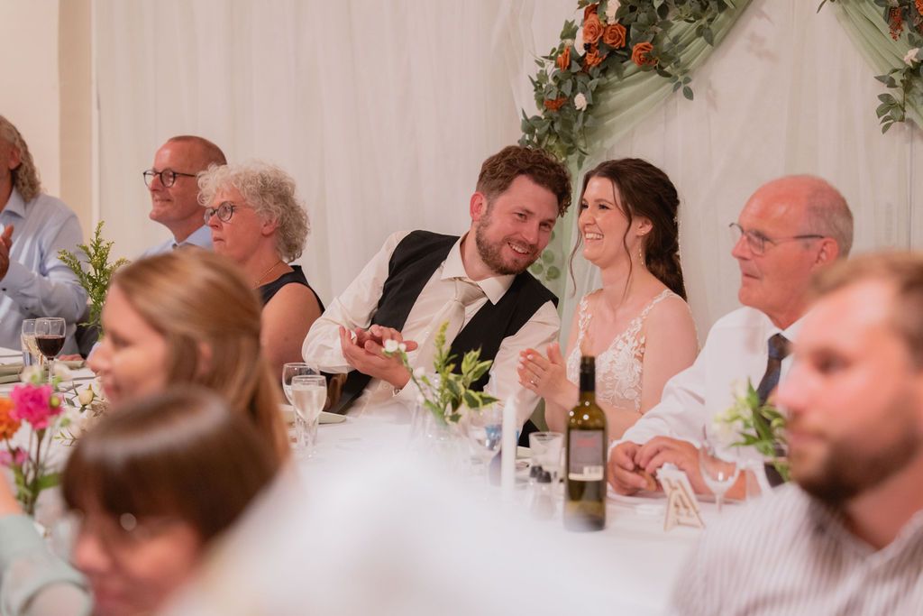 Wedding reception guests seated at decorated tables with floral arrangements.