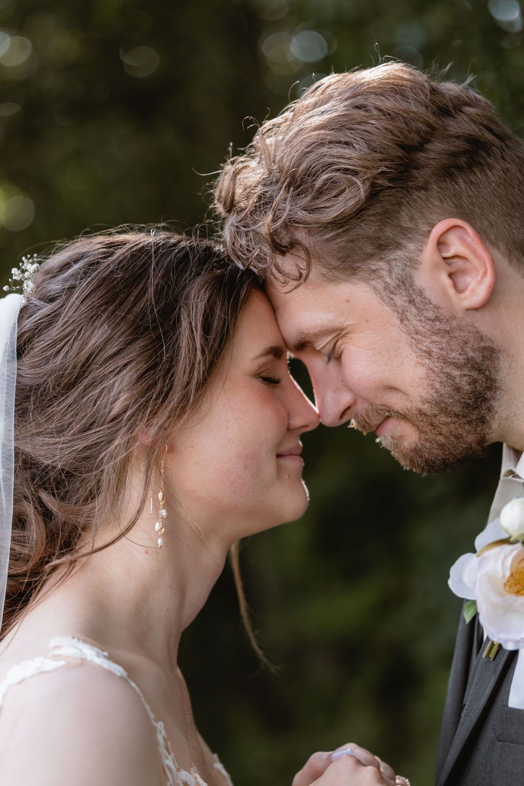 Intimate close-up of wedding couple touching foreheads in romantic outdoor setting.