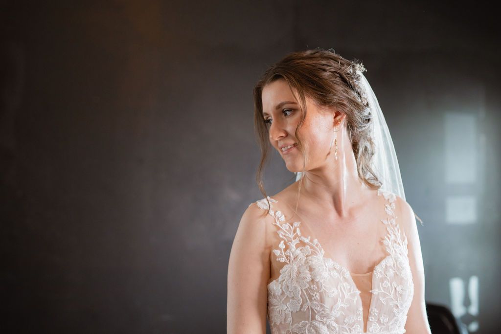 A bride in an elegant lace wedding dress poses during pre-ceremony preparations.