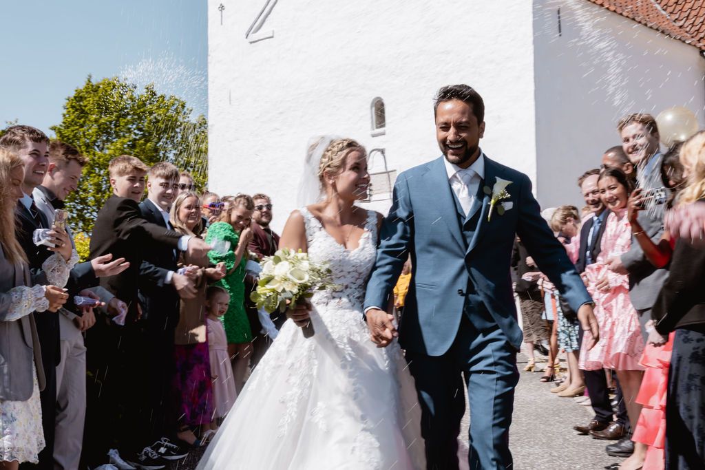 Newlyweds exit their wedding ceremony while guests line the pathway outside a white church.