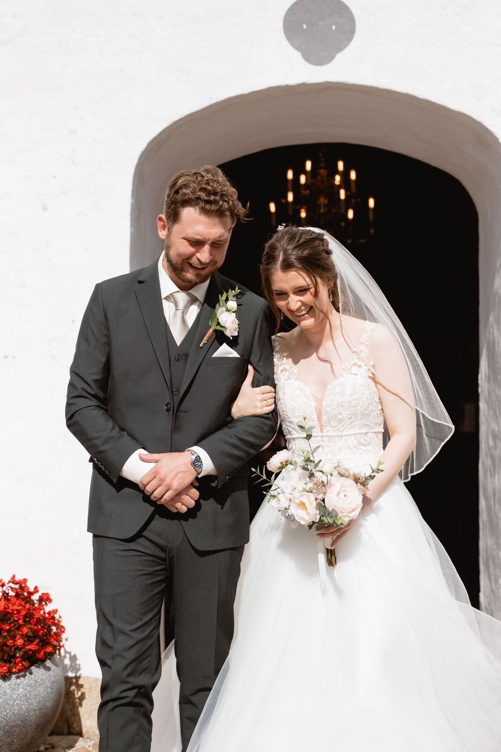 Couple shares romantic moments under white archways decorated with red flowers.