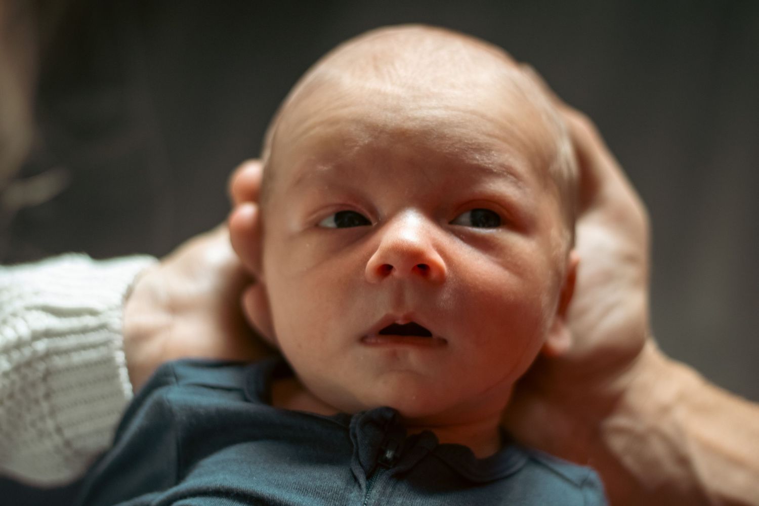 Newborn baby with wide eyes being cradled in loving hands shortly after birth.