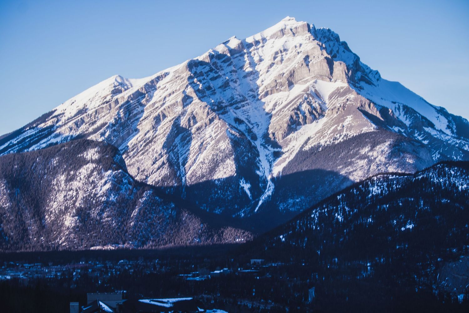 Snow-capped mountain peak under clear blue sky in Banff National Park during winter.