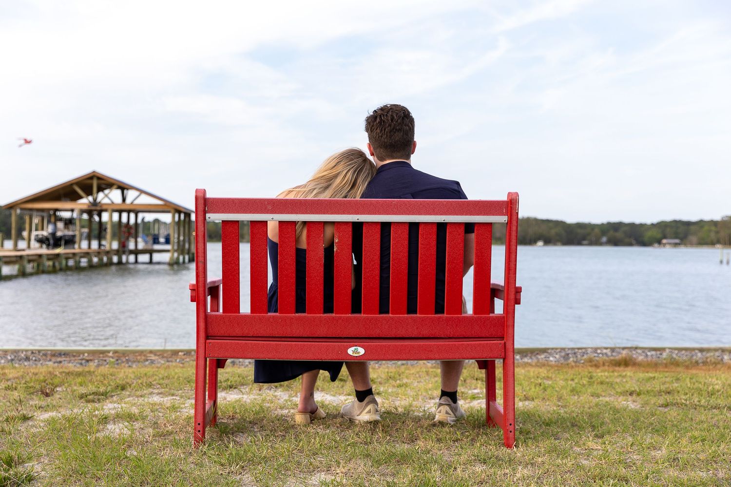Couple sitting together on a red bench overlooking a peaceful lakeside dock.