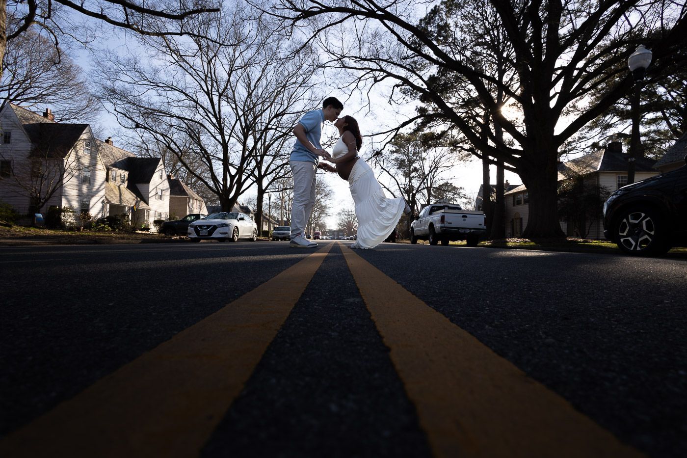 Romantic couple sharing a dip kiss on a street centerline, silhouetted against bare winter trees.