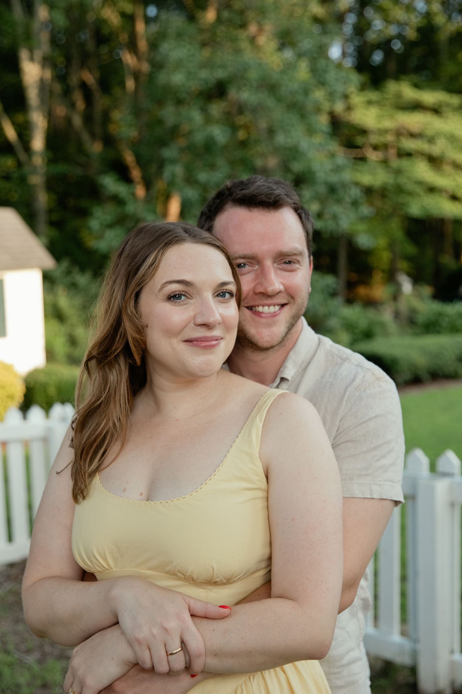 Couple embracing outdoors in a lush garden, woman in yellow dress smiling warmly.