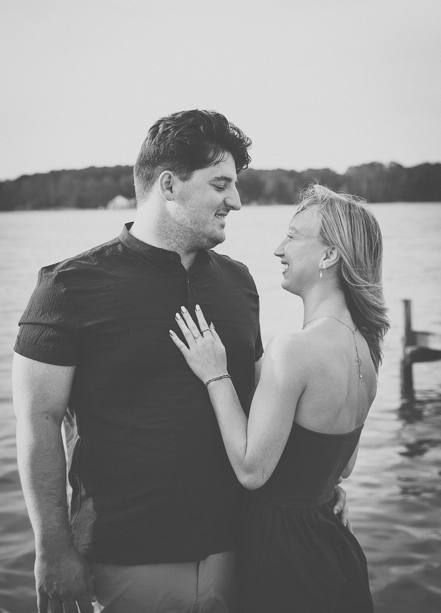 Black and white photo of a smiling couple standing together near a lake shore.