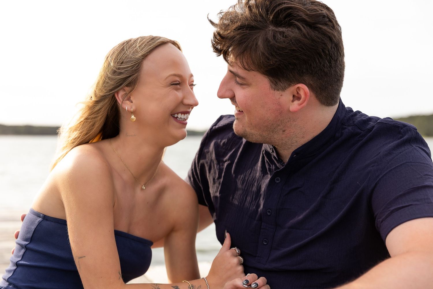 Couple laughing and smiling together on a beach, wearing navy blue outfits with ocean in the background.
