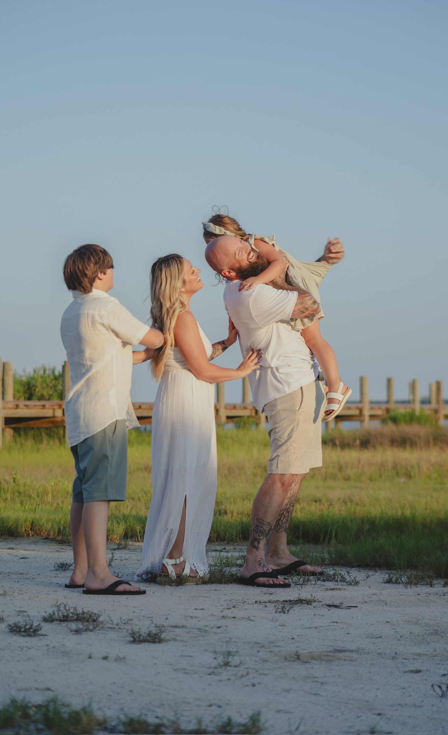 Family of four in white outfits sharing a joyful moment on a sandy beach at golden hour.