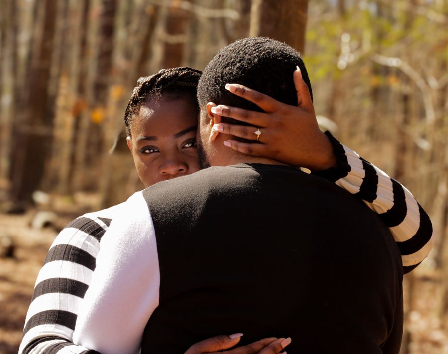 Two people sharing a warm embrace outdoors in a woodland setting during autumn.