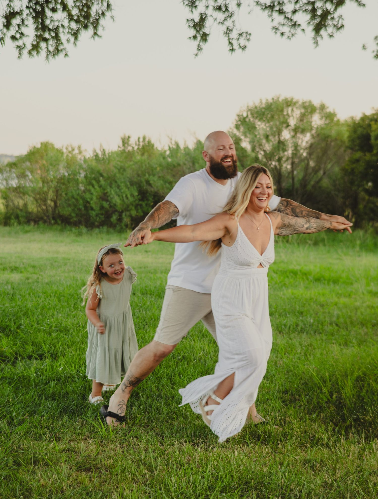 mom and dad playing airplane while daughter follows close behind laughing