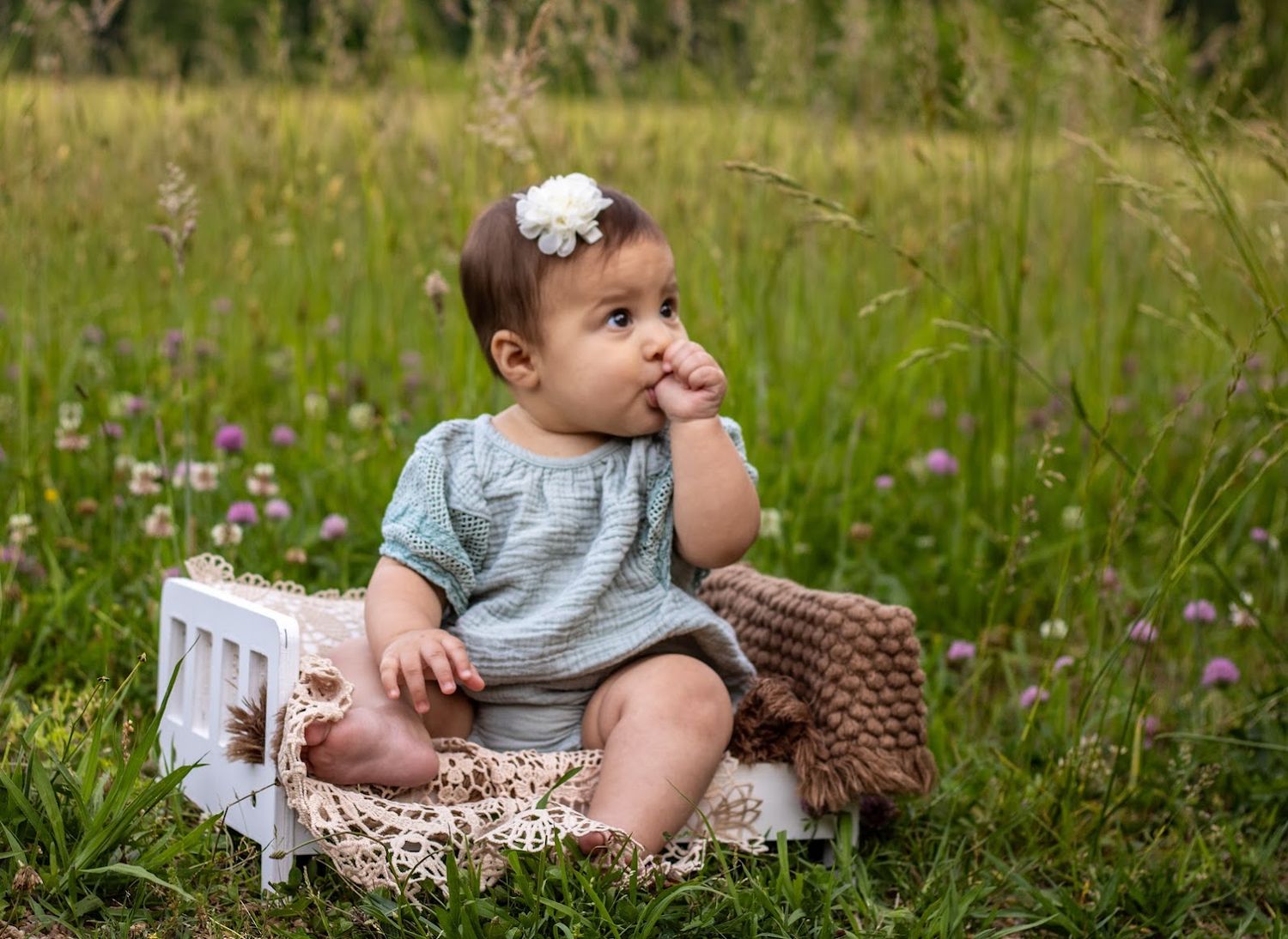 baby girl sucking thumb wearing a sage green rompere on a baby bench in the battlefields of yorktown virginia