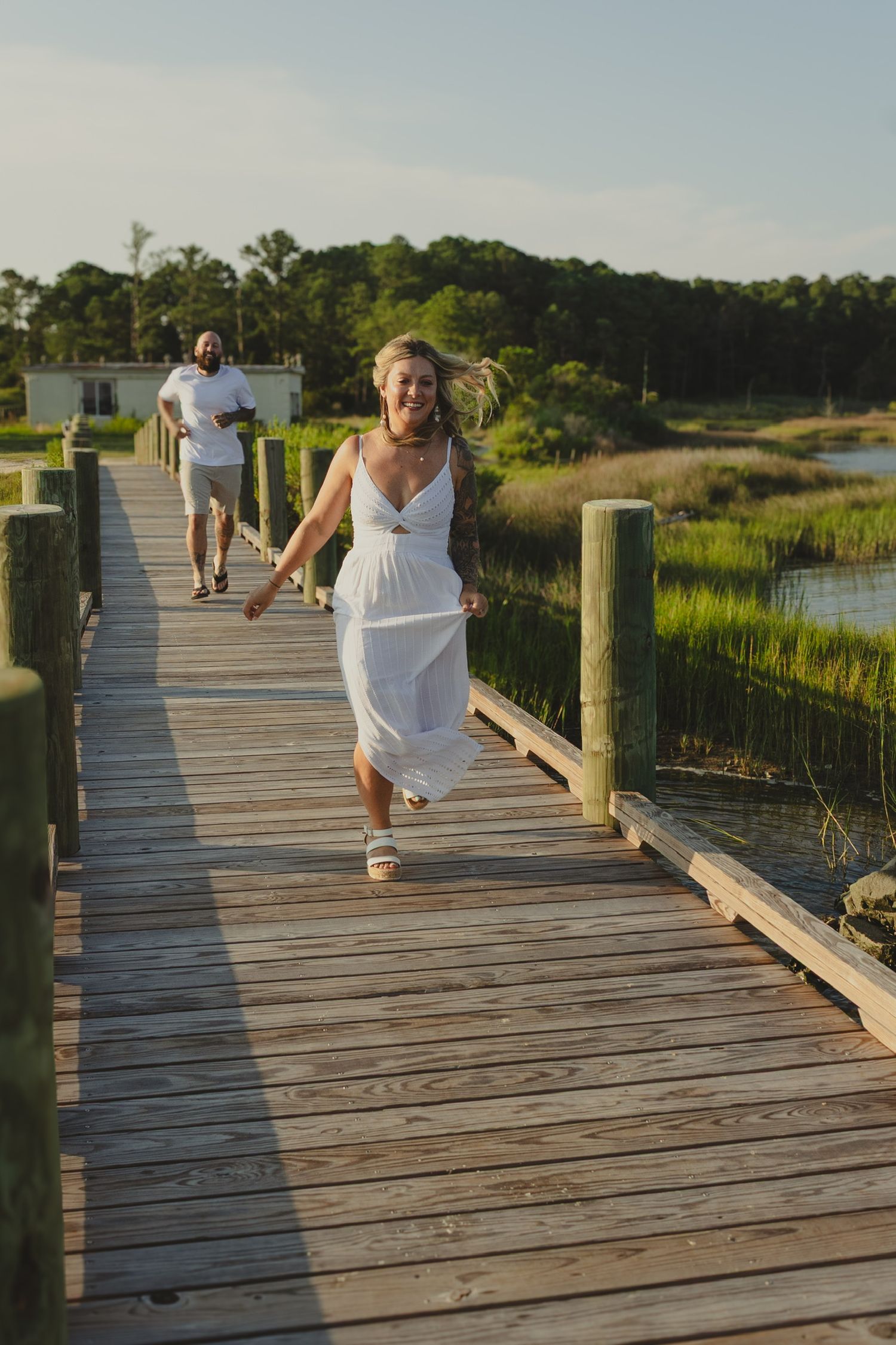 a man chasing a woman down a pier smiling both wearing white