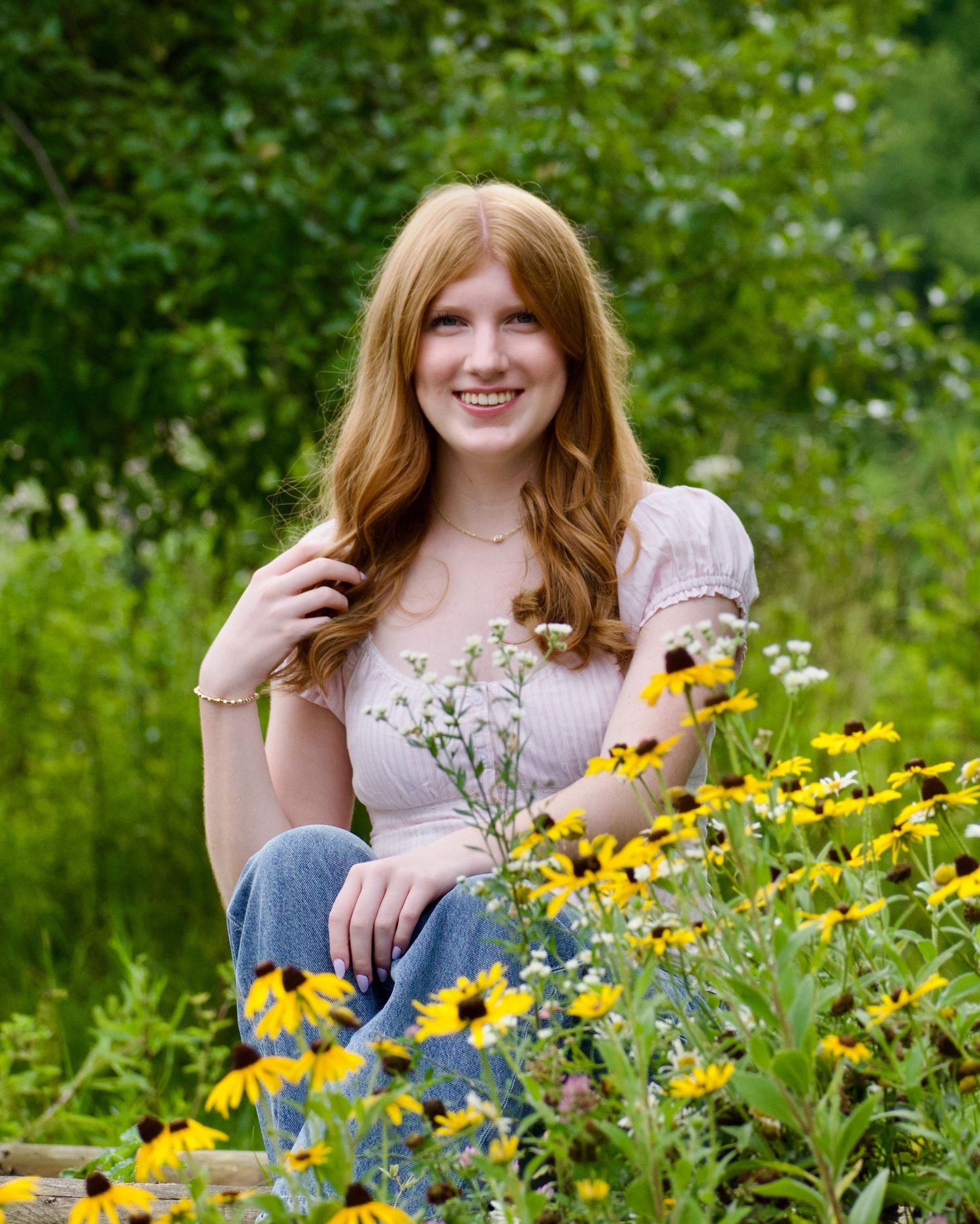 Young woman with red hair sitting among yellow black-eyed Susan flowers in a lush green garden.