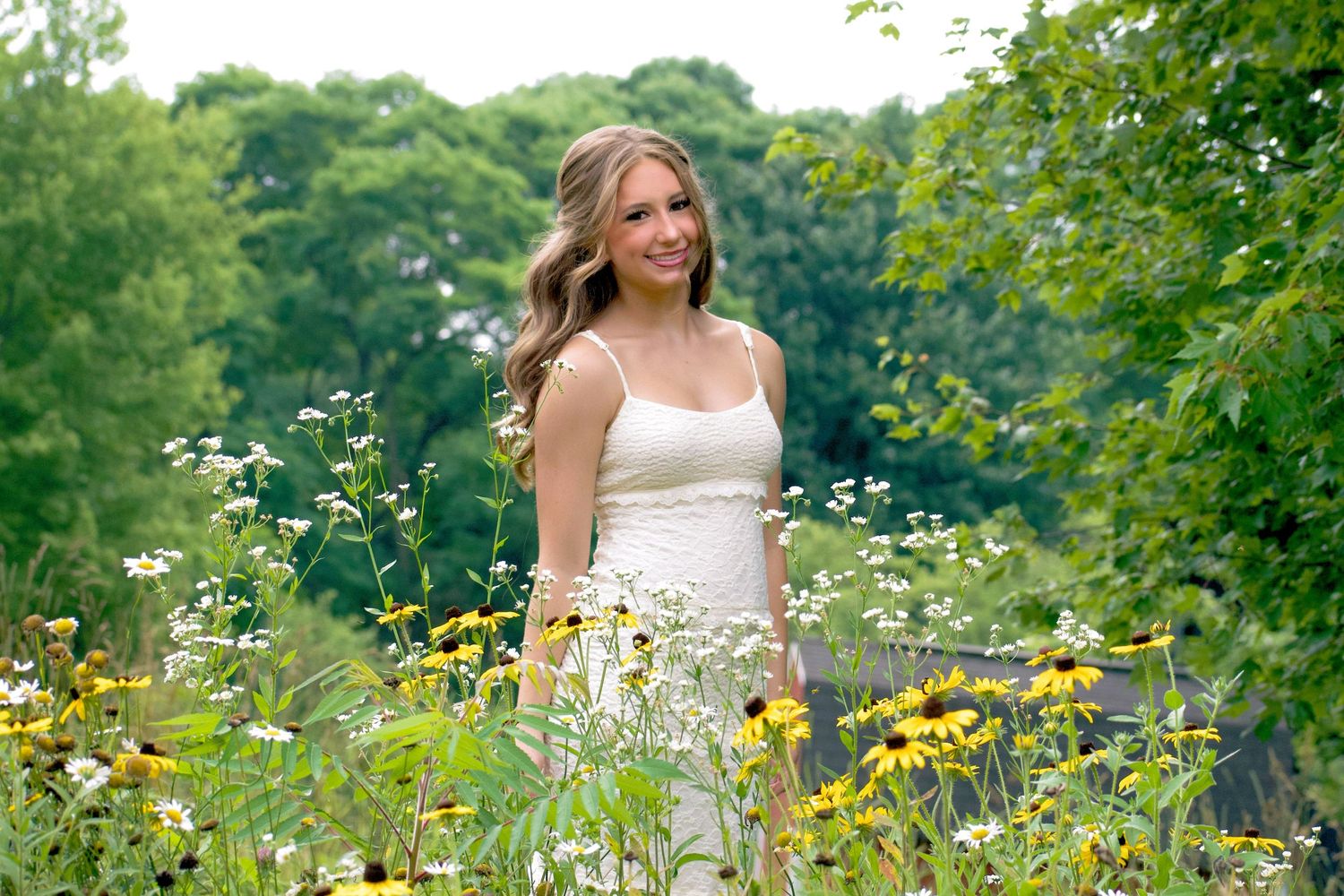Young woman in white dress standing among wildflowers and yellow blooms in a lush green garden.