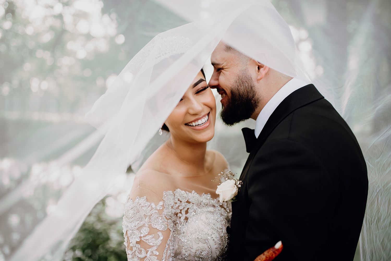 A bride and groom share a romantic moment under a flowing veil on their wedding day.