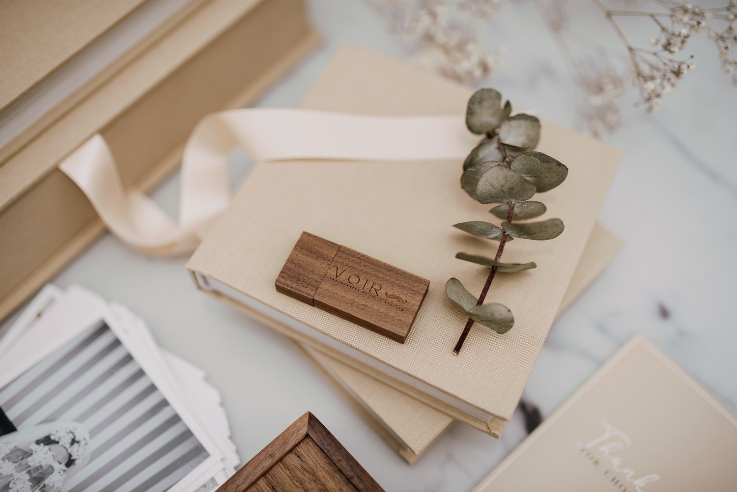 Elegant wedding photography package with linen albums, wooden USB drive, eucalyptus sprig on marble.