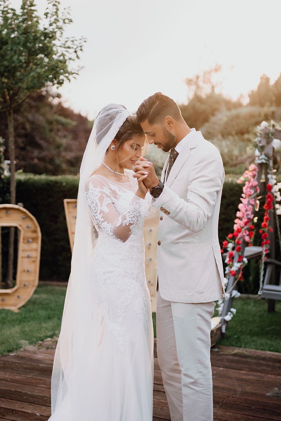 Intimate wedding moment as bride in lace gown and groom in white suit bow heads together outdoors.