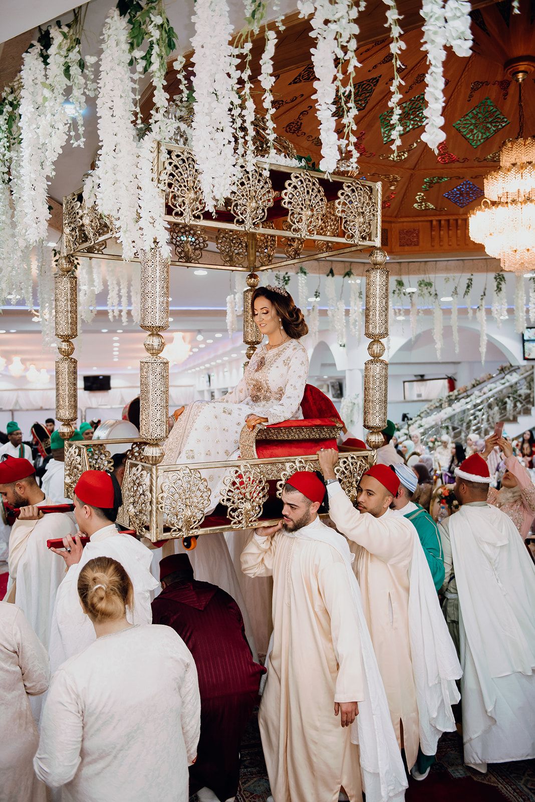 Bride in white lace gown is carried on a traditional Moroccan Amaria throne during wedding ceremony.