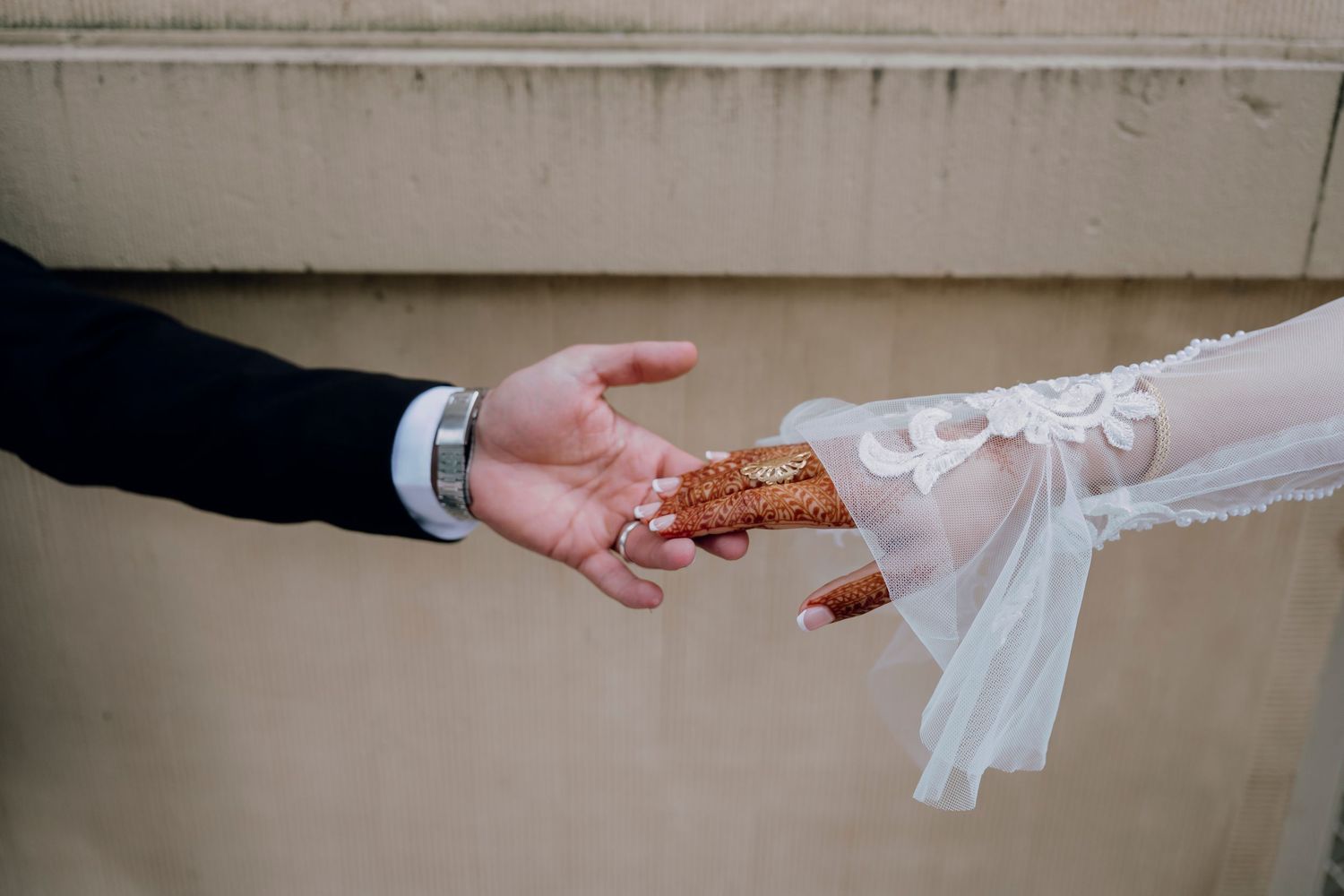 Bride and groom exchange rings, with intricate henna on the bride's hand and a lace wedding dress sleeve.
