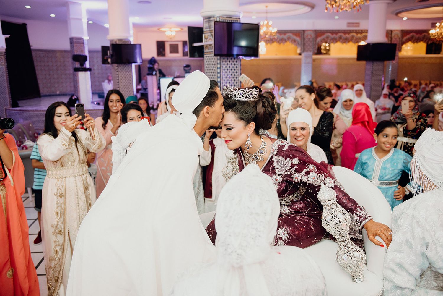 Colorful wedding celebration with guests surrounding a bride in a burgundy embroidered gown.