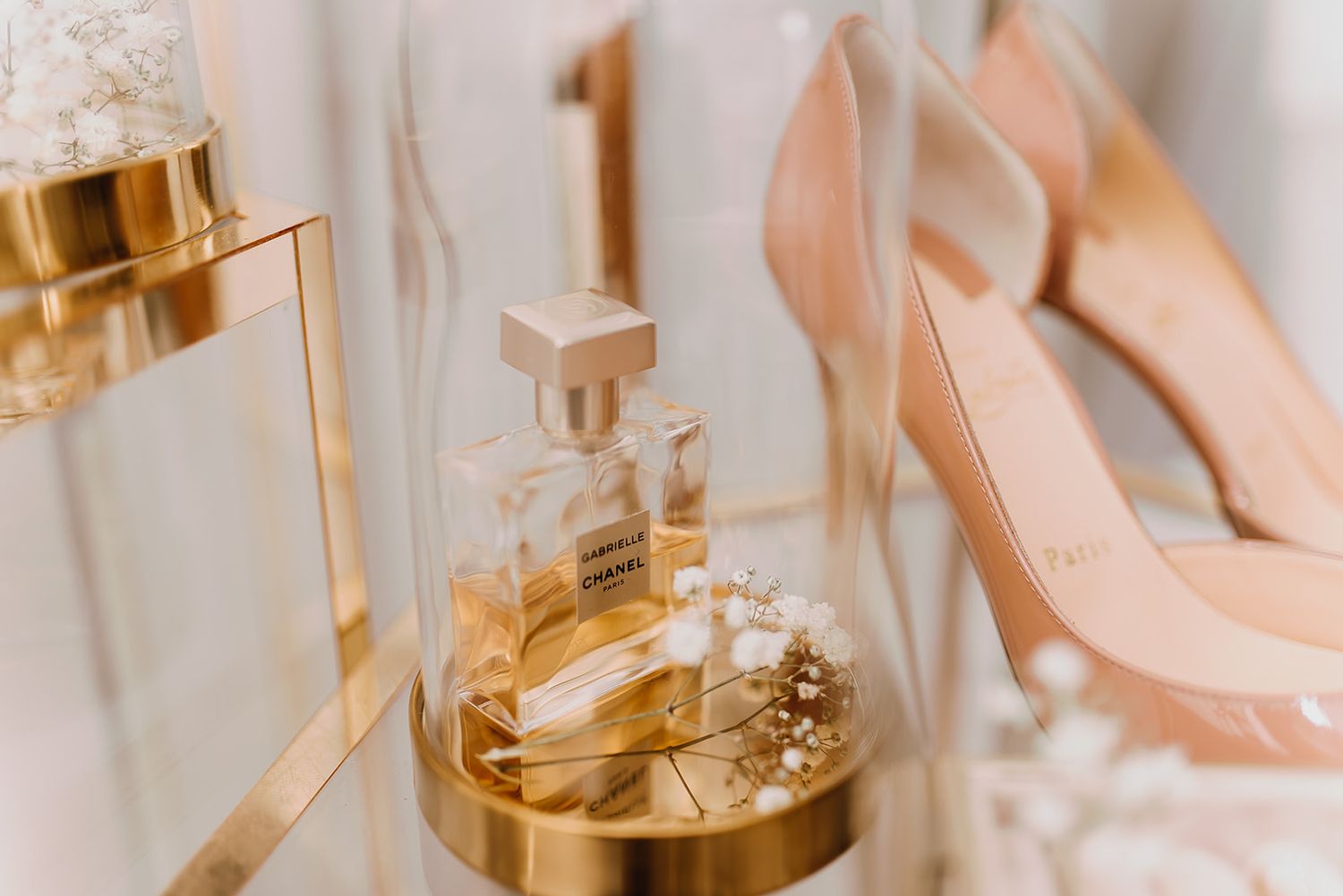 Nude high heel shoes beside a Chanel perfume bottle and gold accessories on display.