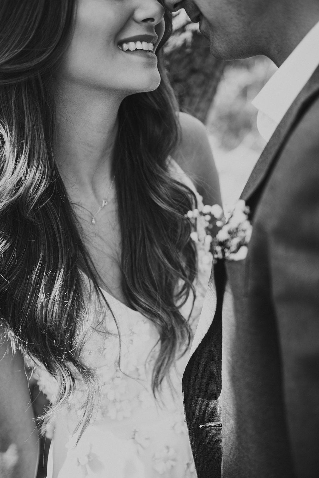 Black and white close-up of smiling bride with long hair beside groom with floral boutonniere.