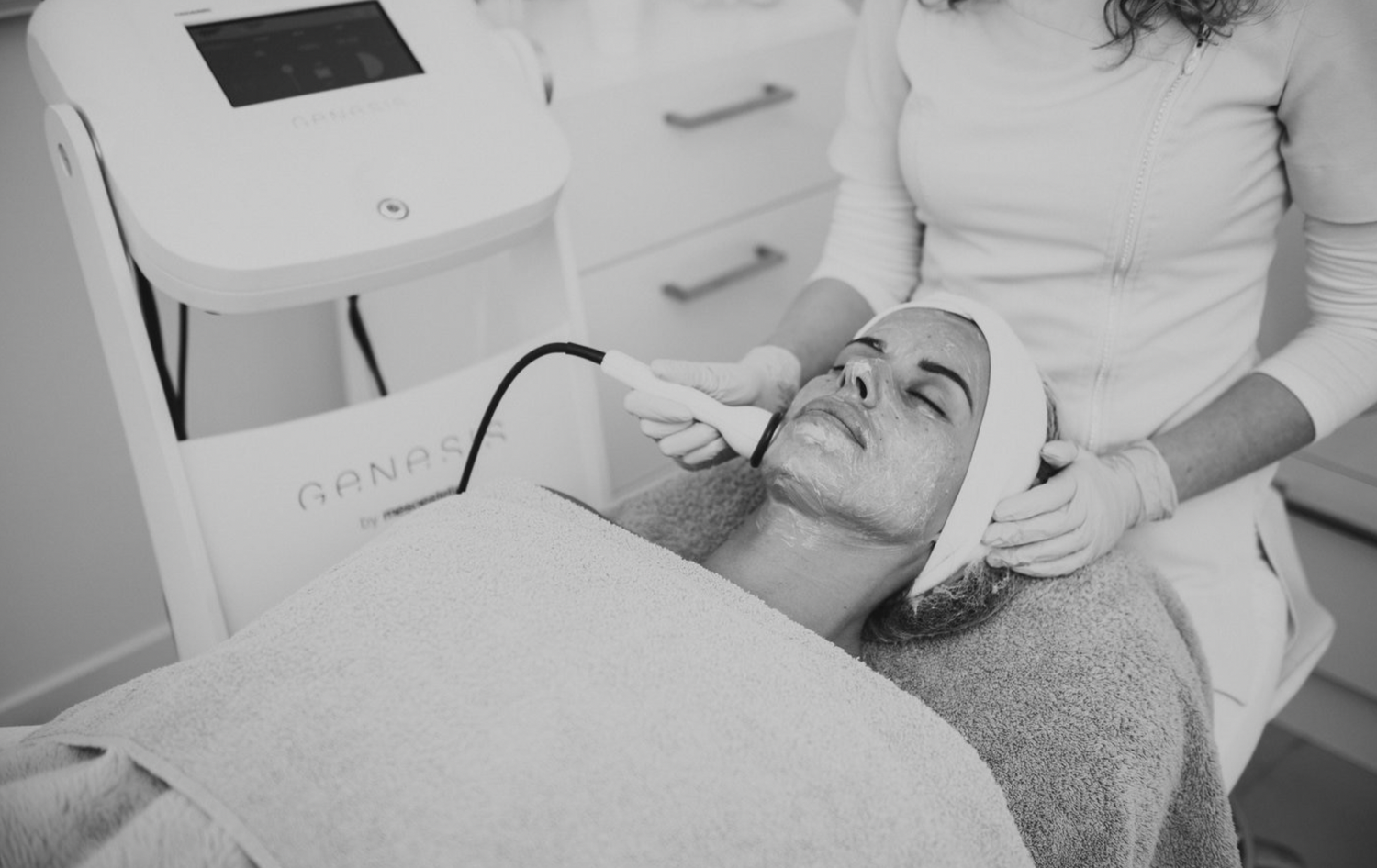 Black and white photo of a woman receiving a professional facial treatment at a beauty clinic.